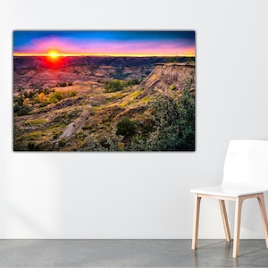 May include: A vibrant sunset over a canyon landscape with a red sky and a bright orange sun. The canyon is covered in green and brown vegetation.