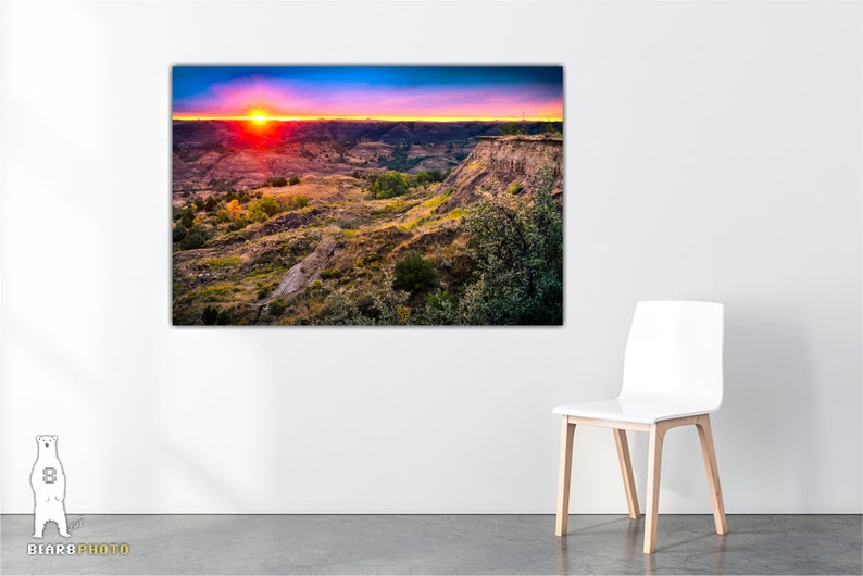 May include: A vibrant sunset over a canyon landscape with a red sky and a bright orange sun. The canyon is covered in green and brown vegetation.