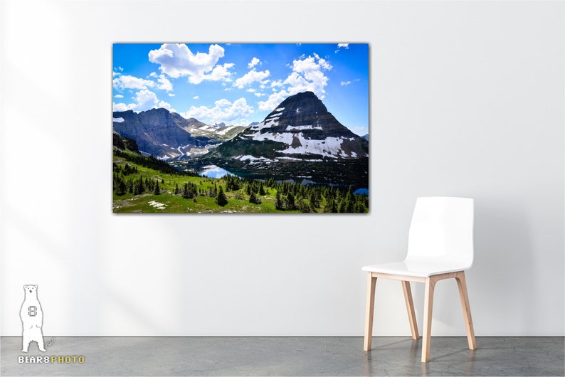 May include: A scenic landscape photograph featuring a mountain range with snow-capped peaks, a valley with a lake, and a blue sky with white clouds.