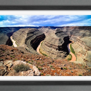May include: An aerial view of a winding river carving through a canyon in a desert landscape. The river is a light brown color and the canyon walls are a mix of brown, tan, and green.