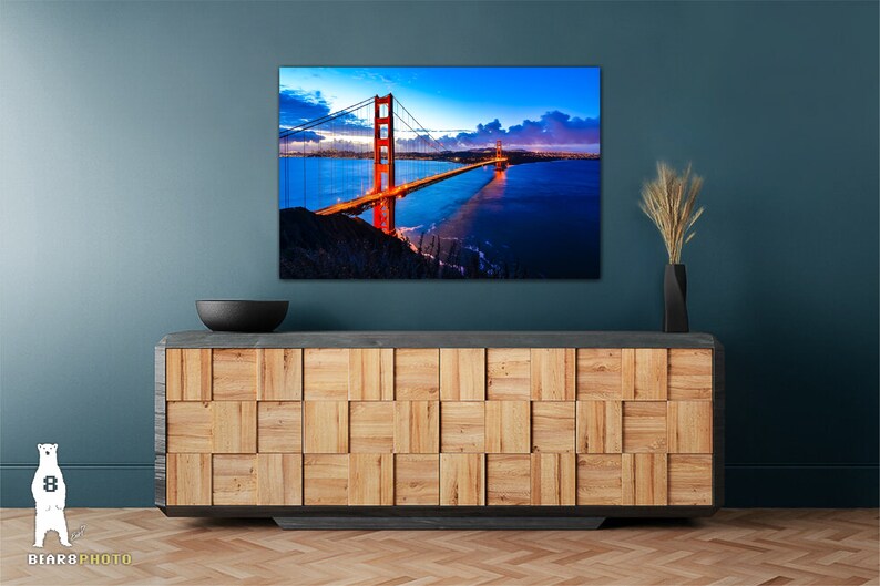 May include: A photograph of the Golden Gate Bridge in San Francisco, California. The bridge is lit up in the evening, and the water is calm and reflective. The sky is a deep blue, and there are clouds in the distance.