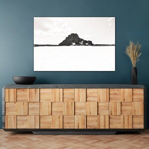 May include: A black and white landscape photograph of a mountain and snow scene. The artwork is displayed above a wooden cabinet with a black bowl and a black vase with dried plants. The cabinet has a geometric design.