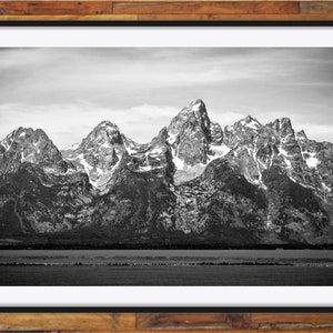 May include: A black and white photograph of a mountain range with snow-capped peaks. The mountains are in the background, and a body of water is in the foreground.