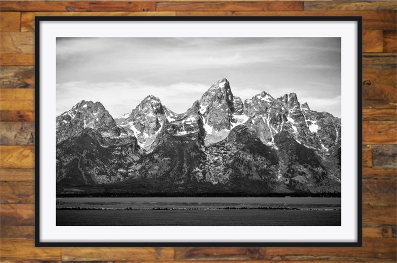 May include: A black and white photograph of a mountain range with snow-capped peaks. The mountains are in the background, and a body of water is in the foreground.