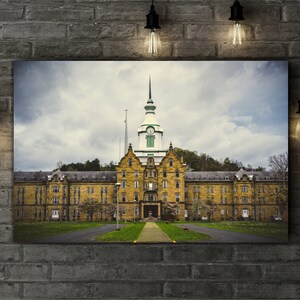 May include: A large, yellow brick building with a green roof and a tall, white spire. The building has many windows and is surrounded by trees and grass.