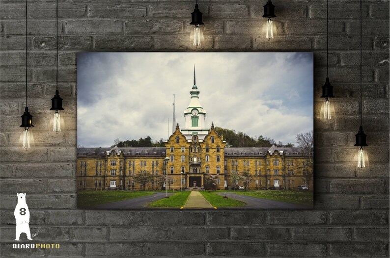 May include: A large, yellow brick building with a green roof and a tall, white spire. The building has many windows and is surrounded by trees and grass.