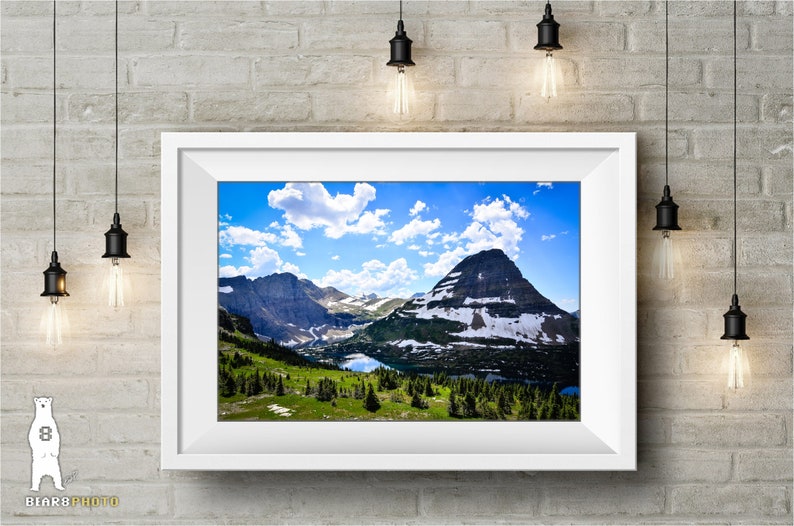 May include: A framed photograph of a mountain range with a blue sky and white clouds. The mountains are covered in snow and green trees. A lake is visible in the valley.