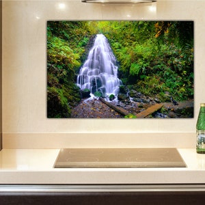 May include: A photograph of a waterfall cascading down a rocky cliff, surrounded by lush green foliage. The water is clear and white, and the rocks are brown and gray. The foliage is a mix of green leaves and ferns.