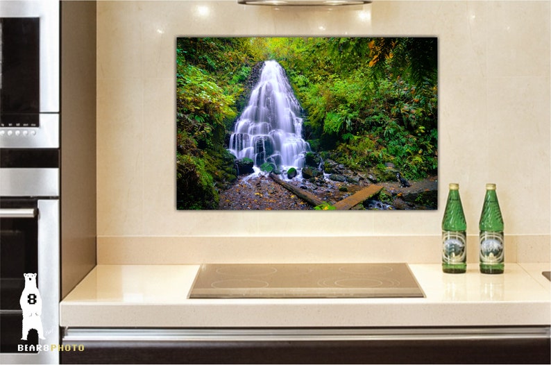 May include: A photograph of a waterfall cascading down a rocky cliff, surrounded by lush green foliage. The water is clear and white, and the rocks are brown and gray. The foliage is a mix of green leaves and ferns.