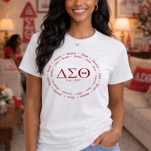 May include: White t-shirt with a maroon circular design featuring names and the Greek letters ΔΣΘ. The text "Est. 1913" is below the Greek letters. The person is wearing blue jeans.
