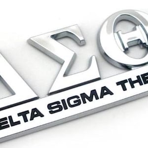 May include: A shiny, silver emblem featuring the Greek letters Delta, Sigma, and Theta, with the words DELTA SIGMA THETA in bold, black capital letters. The emblem is likely a sorority symbol.