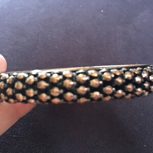 Op de afbeelding: Een ronde armband van metaal in goud en zwart met een textuur.