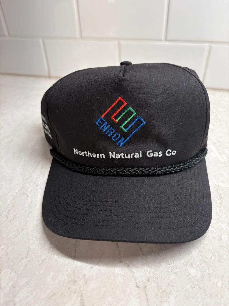 Pu&ograve; includere: Cappellino da baseball nero con il logo Enron ricamato in rosso, verde e blu. Il testo "Northern Natural Gas Co" &egrave; ricamato in bianco. Il cappellino ha un dettaglio di corda nera lungo la tesa.