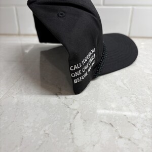 Pu&ograve; includere: Cappellino da baseball nero con testo ricamato bianco: "CALL YOUR LOCAL ONE CALL CENTER BEFORE YOU DIG". Il cappellino ha una visiera curva e un dettaglio intrecciato sul bordo.