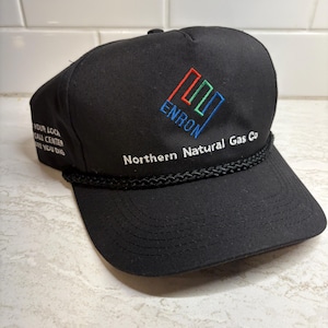 Pu&ograve; includere: Cappellino da baseball nero con la scritta ricamata "ENRON" in blu, rosso e verde, e le parole "Northern Natural Gas Co" in bianco. Il cappellino presenta anche il testo "YOUR LOCAL CALL CENTER BEFORE YOU DIG".