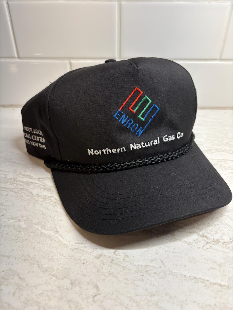 Pu&ograve; includere: Cappellino da baseball nero con la scritta ricamata "ENRON" in blu, rosso e verde, e le parole "Northern Natural Gas Co" in bianco. Il cappellino presenta anche il testo "YOUR LOCAL CALL CENTER BEFORE YOU DIG".