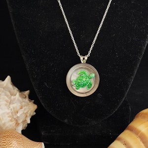 May include: Silver chain necklace with a round pendant featuring a green turtle inside a clear glass dome.