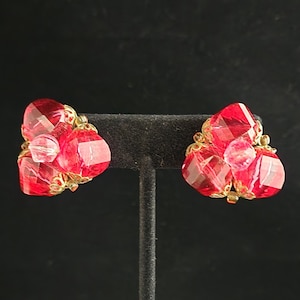 Peut inclure: Une paire de boucles d'oreilles en grappe de verre rouge sur un support noir. Les boucles d'oreilles sont composées de plusieurs petites perles de verre rouge facettées.