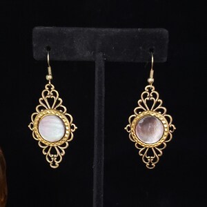 May include: A pair of gold filigree earrings with a round iridescent white shell center.