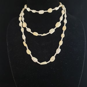Puede incluir: Un collar de varias hebras hecho de cuentas de concha blanca ovaladas con detalles plateados.