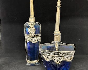 May include: Two cobalt blue glass perfume bottles with silver accents and ornate designs. The bottles have long, slender necks and are decorated with intricate patterns.
