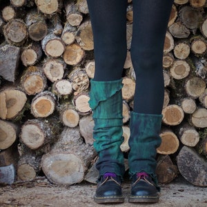 Può includere: Un paio di scaldagambe color teal e nero con un bordo arricciato. Gli scaldagambe sono indossati con leggings neri e scarpe nere.