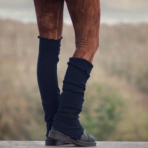 Könnte beinhalten: Ein Paar schwarze Beinstulpen mit einem Rüschenrand. Die Beinstulpen werden über einer braunen Leggings getragen.