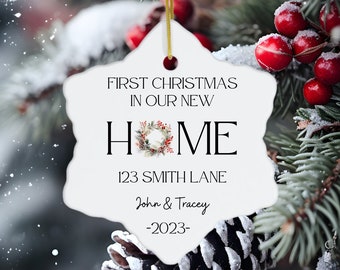 Pode incluir: Adorno de Natal de cerâmica branca em forma de estrela com o texto "First Christmas in our new HOME 123 Smith Lane John & Tracey -2023- ". O adorno tem uma coroa com bagas vermelhas e folhas verdes no "O" de HOME. O adorno está pendurado em um galho de pinheiro nevado com bagas vermelhas.