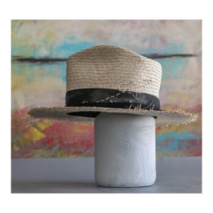 May include: A straw hat with a black band and a safety pin. The hat is sitting on a white painted jar.