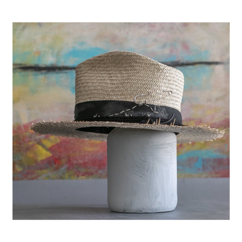 May include: A straw hat with a black band and a safety pin. The hat is sitting on a white painted jar.