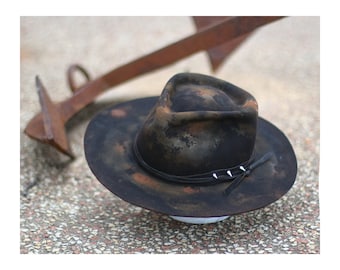 May include: A black felt fedora hat with a brown and black mottled pattern. The hat has a leather band with silver studs and a leather tie.