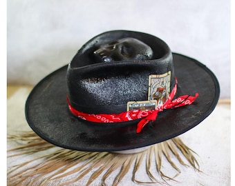 May include: Black fedora hat with a skull design on the crown. The hat has a red bandana wrapped around the brim and a small card with the text "Keep it real" attached to the front.