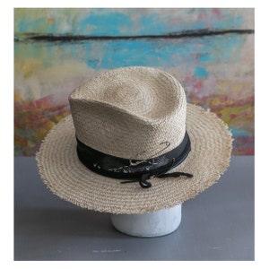 May include: A straw hat with a wide brim and a black band. The hat has a frayed edge and a safety pin attached to the band.