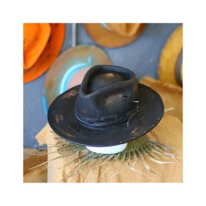 Può includere: Un cappello fedora grigio antracite scuro con una finitura usurata e invecchiata. Il cappello presenta una corona pizzicata, una tesa larga con borchie metalliche lungo il bordo e una sottile fascia in pelle scura attorno alla base.