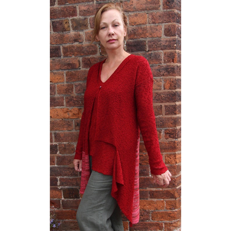 May include: A red, long-sleeved, asymmetrical sweater with a V-neck and a textured knit. The sweater has a longer hem in the back and a shorter hem in the front.