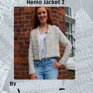 May include: A woman wearing a white and blue patterned cropped jacket with a fringe trim. The jacket has a gold button on the front. The woman is standing in front of a brick wall. The text "Machine Knitting Patterns Designer Knitwear Henio Jacket 2" is at the top of the image. The text "By henio Handcrafted Designer Knitwear Pattern Series" is at the bottom of the image.