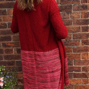 May include: A red and pink knitted cardigan with a long, flowing design. The cardigan is worn over white pants.
