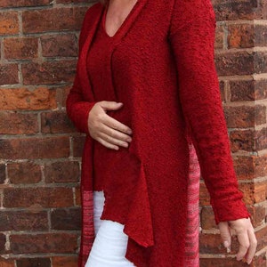 May include: A woman wearing a red, long-sleeved, open-front cardigan with a white, high-waisted, wide-leg pant.