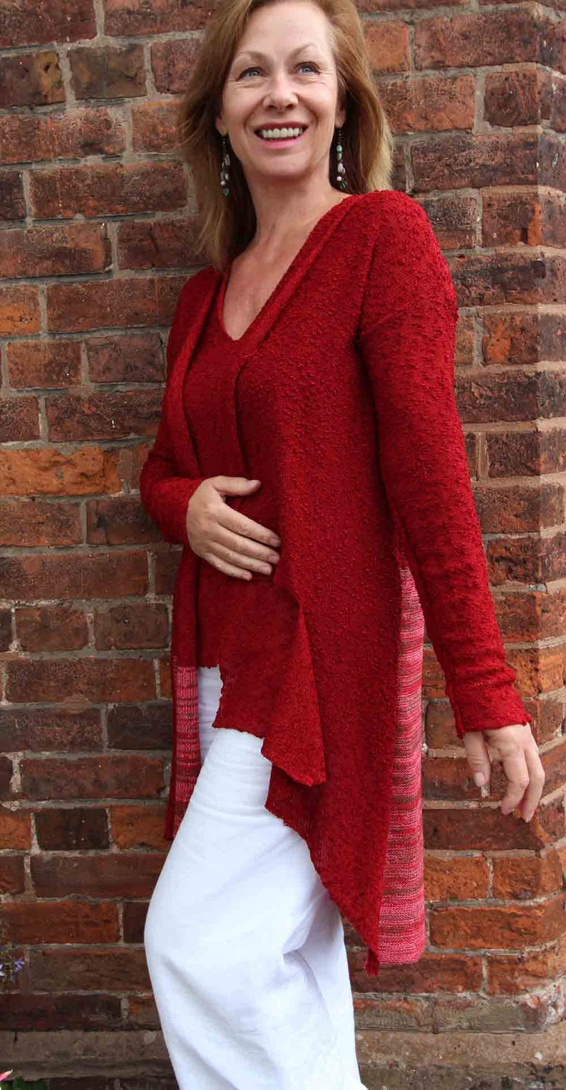 May include: A woman wearing a red, long-sleeved, open-front cardigan with a white, high-waisted, wide-leg pant.