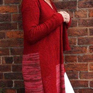 May include: A red knitted cardigan with a long, asymmetrical hemline. The cardigan has a textured knit and a subtle ombre effect in the lower portion.