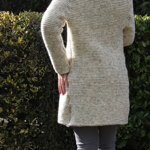 May include: A white knitted cardigan with a long sleeve and a high collar. The cardigan is worn over gray jeans and the person is wearing brown ankle boots.