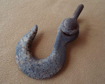 May include: A weathered, dark gray metal hook with a curved design. The hook has a textured surface and a rounded top with a bolt. The item appears to be vintage or antique.