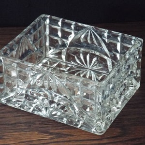 May include: A clear glass rectangular dish with a cut glass design. The dish is empty and has a square shape.