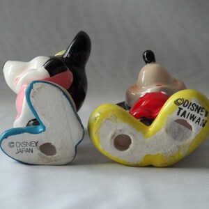 Puede incluir: Dos figuras vintage de Disney. Una es negra, blanca y rosa, con una base azul y el texto "Disney Japan". La otra es amarilla, roja y marr&oacute;n claro, con el texto "Disney Taiwan".