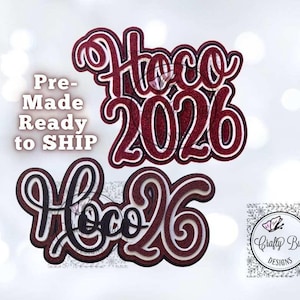 May include: Two layered, decorative toppers with the text "Hoco 2026". The top topper is burgundy glitter with a white outline. The bottom topper is black with a white outline. The image also includes the text "Pre-Made Ready to SHIP" and a logo.