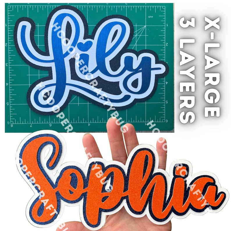 May include: Two layered name cutouts. The top cutout displays the name Lily in blue shades on a green cutting mat with a 6-inch width. The bottom cutout displays the name Sophia in orange and dark blue glitter, labeled as X-LARGE 3 LAYERS.
