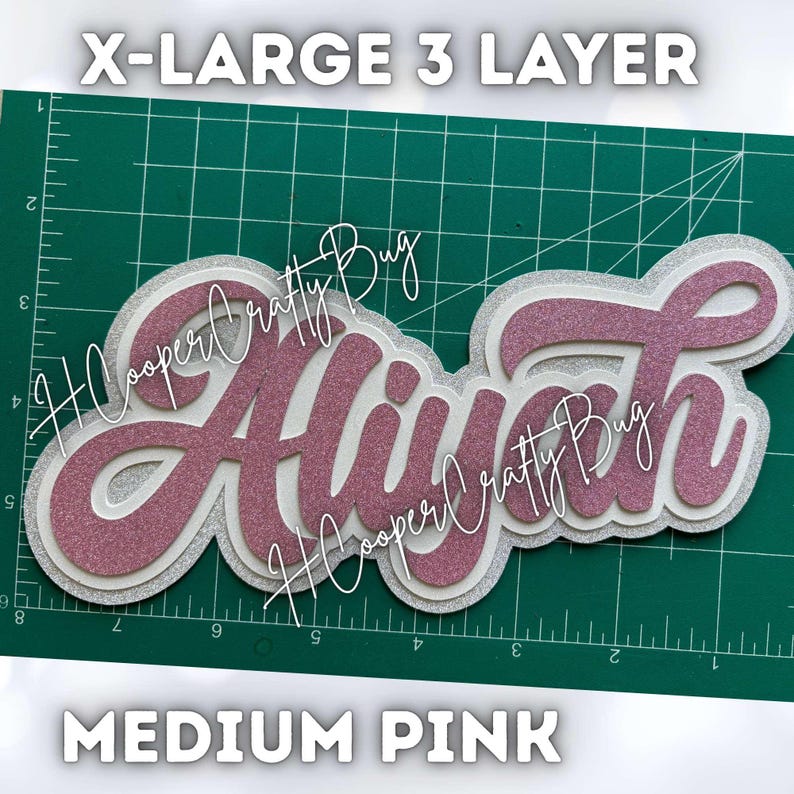 May include: A three-layer custom name cutout featuring the name Aliyah in glittery medium pink script, layered over white and silver glitter cardstock. The text X-LARGE 3 LAYER and MEDIUM PINK is visible, along with a green cutting mat grid.