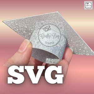 Op de afbeelding: Een zilveren glitter afstudeerhoed-topper met een rond logo met een vlindericoon en de tekst Crafty Bug DESIGNS. Het woord SVG wordt in grote witte letters onderaan de afbeelding weergegeven tegen een achtergrond met kleurverloop.
