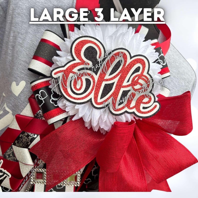 May include: A large 3 layer decorative bow featuring a white ruffled center, red and black glittered lettering that reads "Ellie", and layered ribbons in red, black, and white with various patterns including hearts and geometric shapes.