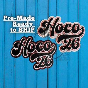 May include: Two black and red glittery "Noco 26" cutouts with white outlines, set against a blue wooden background. The text "Pre-Made Ready... to SHIP" is above the cutouts.